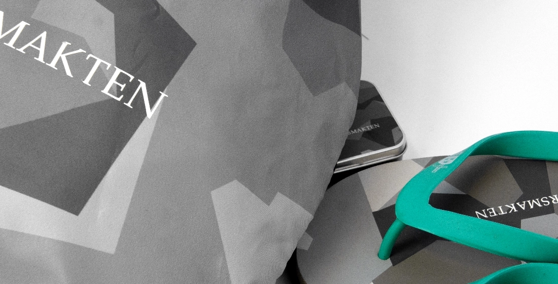 Närbild på Försvarsmaktens merchandise, inklusive flip-flops med turkosa remmar och tyg, som alla har ett grått kamouflage-/geometriskt mönster